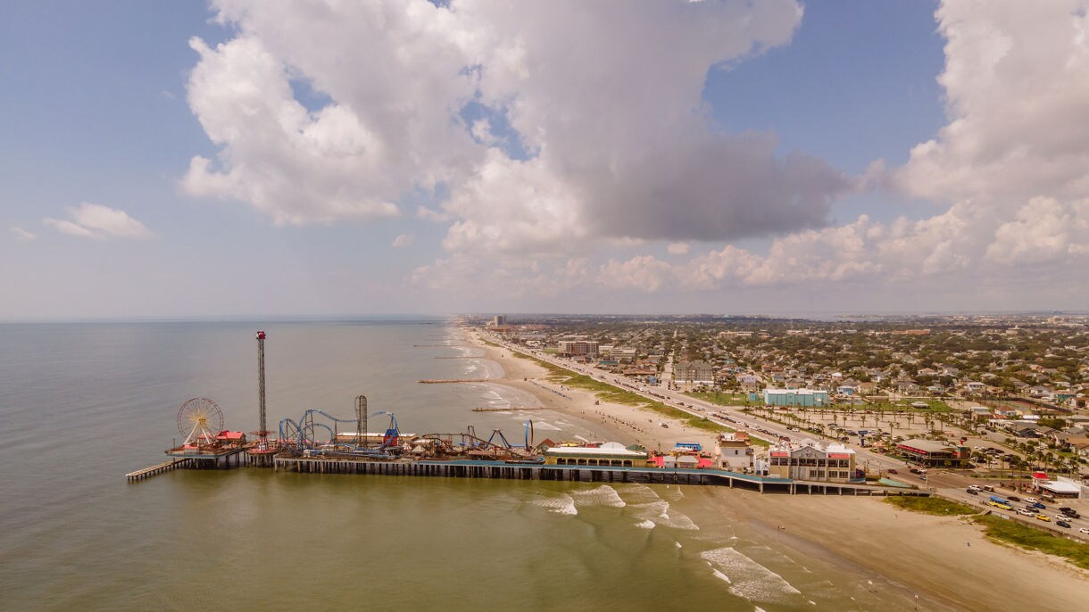 Experience the vibrant energy of the amusement pier, with glowing rides and a stunning sunset sky painting the backdrop.