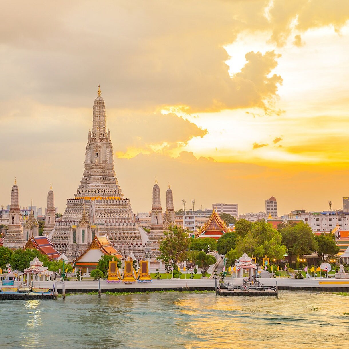 Ornate spires of Wat Arun temple complex in Bangkok, with its central prang towering above the river and traditional Thai rooftops below.