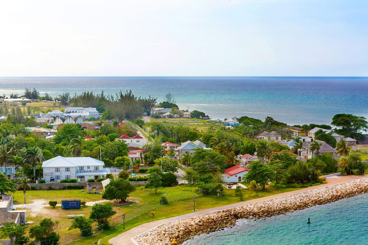 Aerial view of Falmouth Jamaica showing colorful coastal houses with red roofs along turquoise Caribbean waters and stone breakwater.