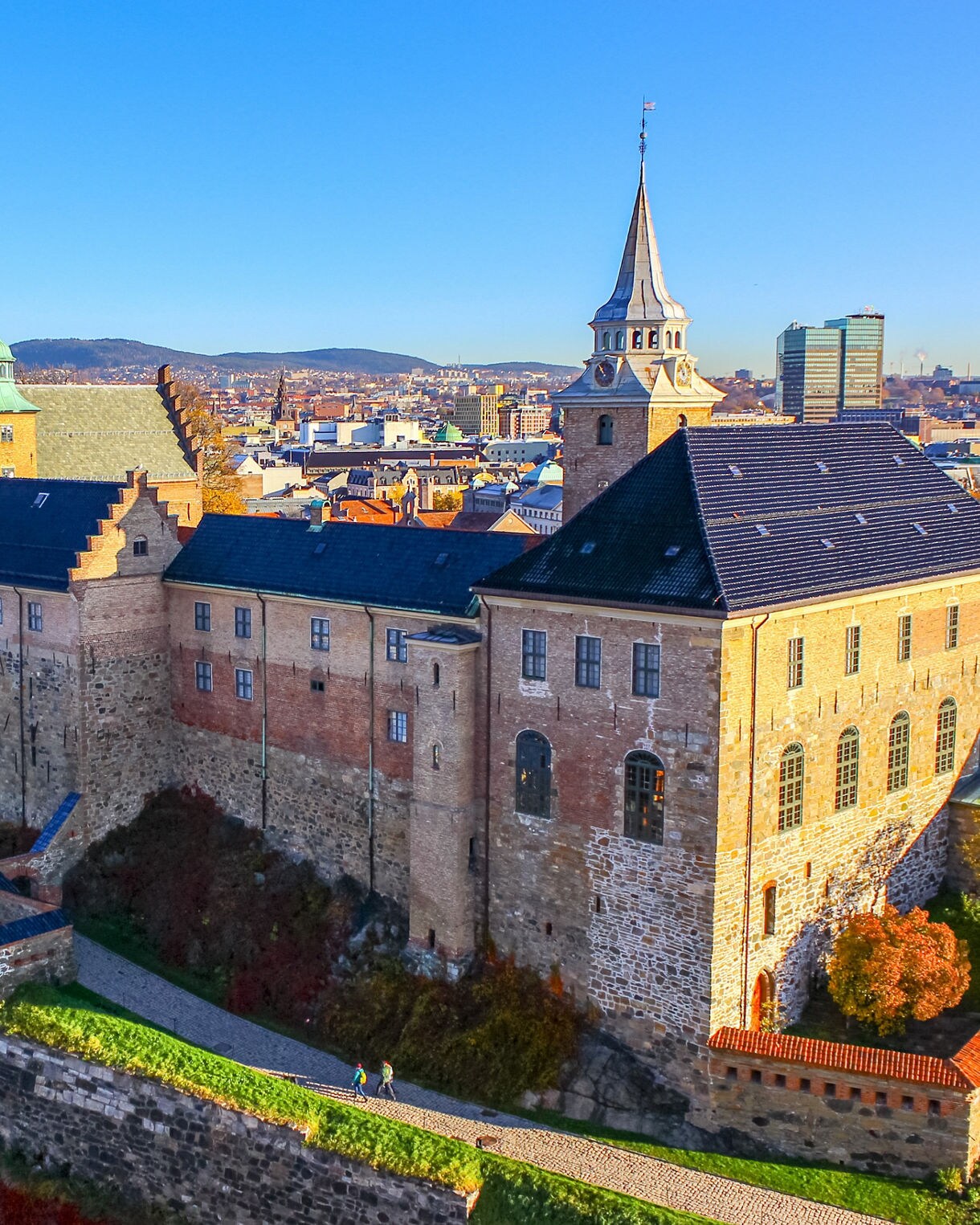 Akershus Fortress in Oslo, Norway, with stone walls, towers and autumn trees surrounding the historic castle against a clear blue sky.