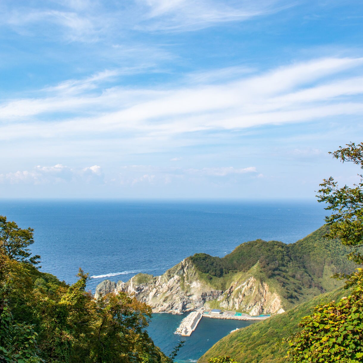 Scenic view of the Oga Peninsula with lush green cliffs and a deep blue ocean under a bright sky.