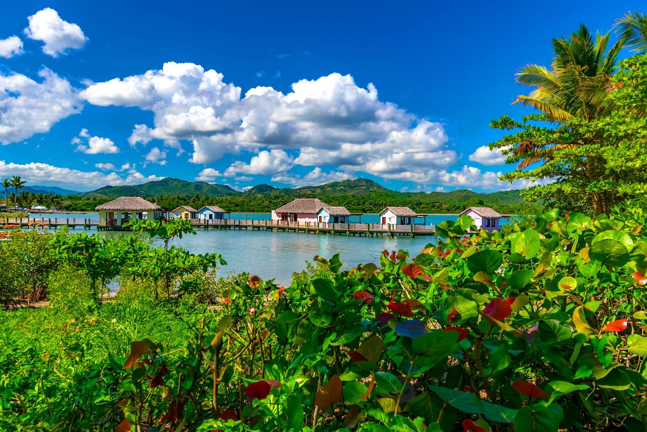 Overwater bungalows with thatched roofs over turquoise Caribbean lagoon near Amber Cove, Dominican Republic.