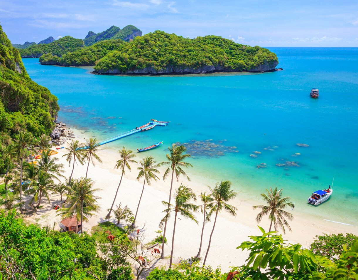 Aerial view of Ang Thong National Marine Park featuring white sand beach, turquoise water, palm trees and small boats near green islands.
