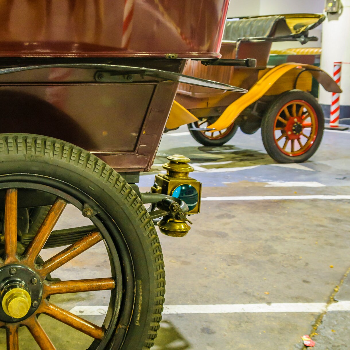 Close-up of vintage cars showing wooden-spoked wheels, brass lanterns and polished bodywork inside a garage.