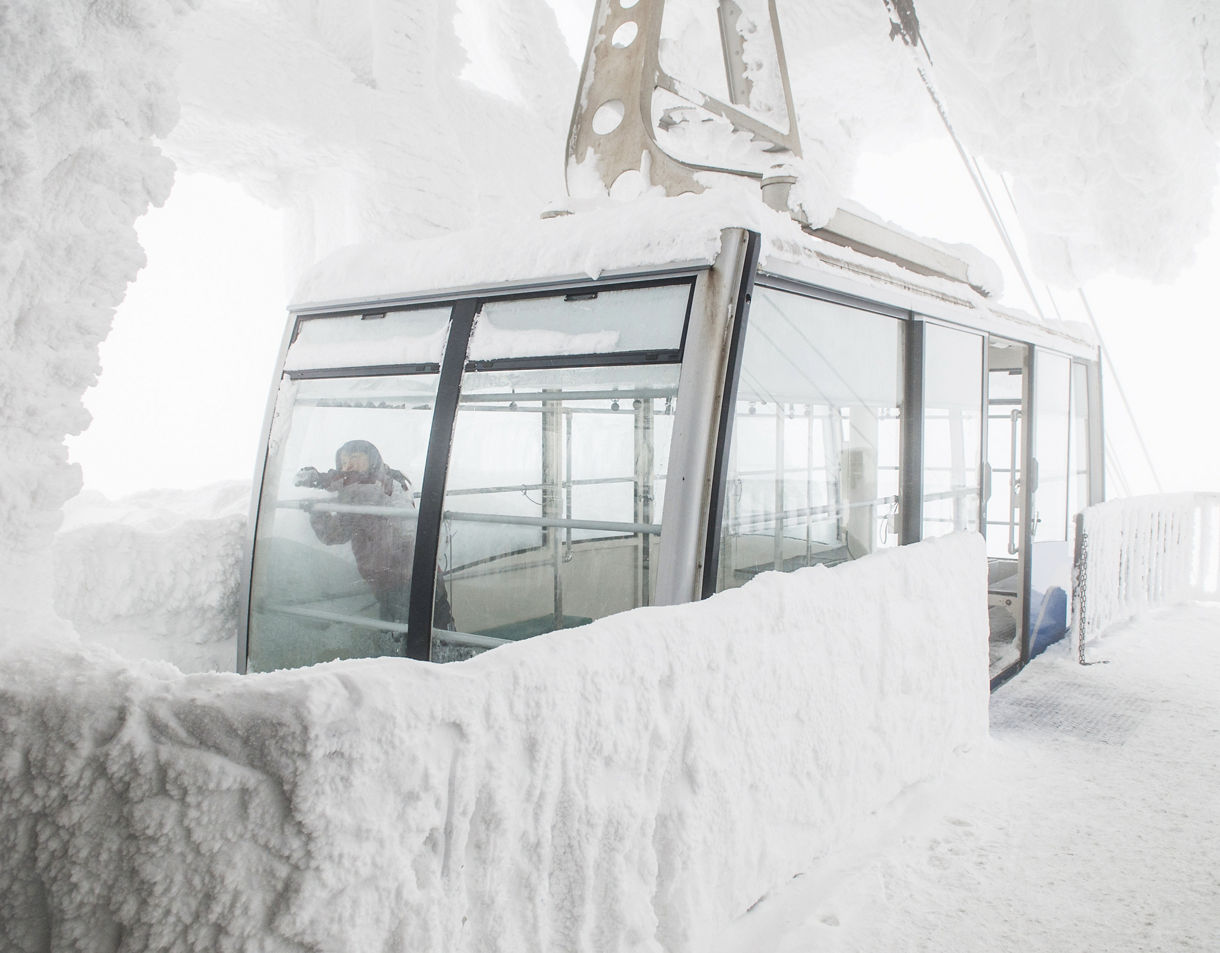 Snow-covered tram at Hakkoda Ropeway station with thick frost on walls and a person inside taking photos.