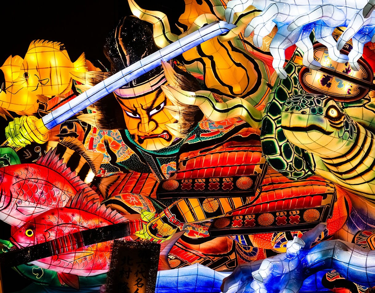 Colorful Nebuta float featuring a fierce samurai with a sword, glowing fish and a turtle, all lit from within. Caption: Aomori, Japan