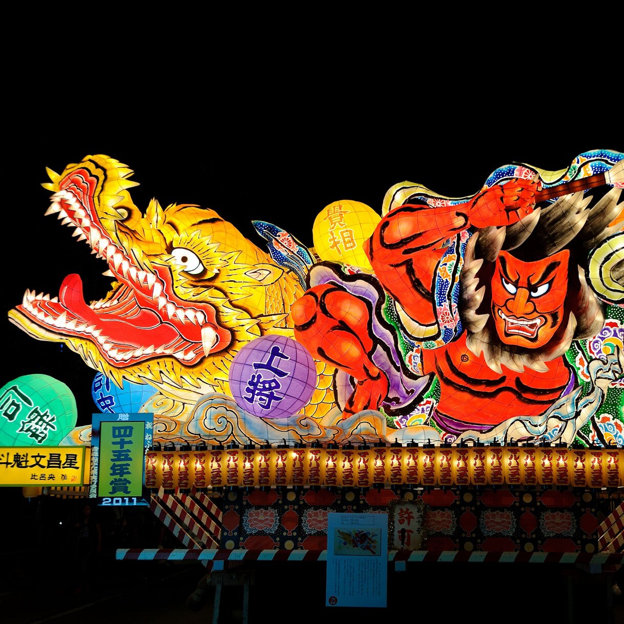 Colorful illuminated float of a fierce warrior and dragon on display indoors.