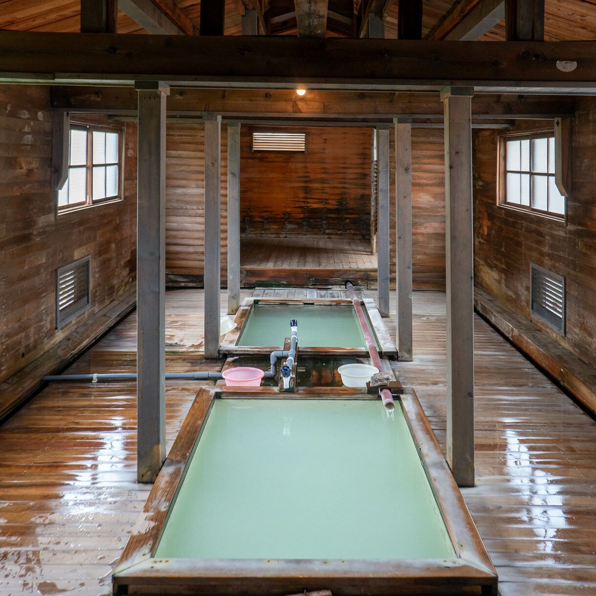 Wooden indoor hot spring bathhouse with milky green mineral water pools.