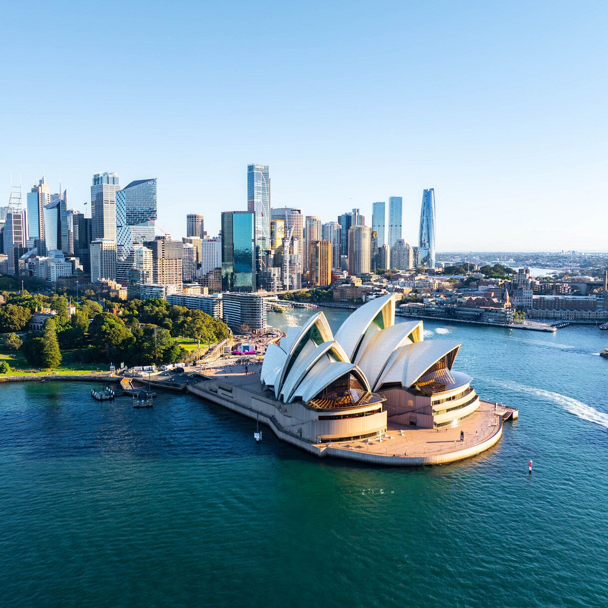 Aerial view of the Sydney Opera House on the harbor, with ferries in the water and the city skyline of skyscrapers behind