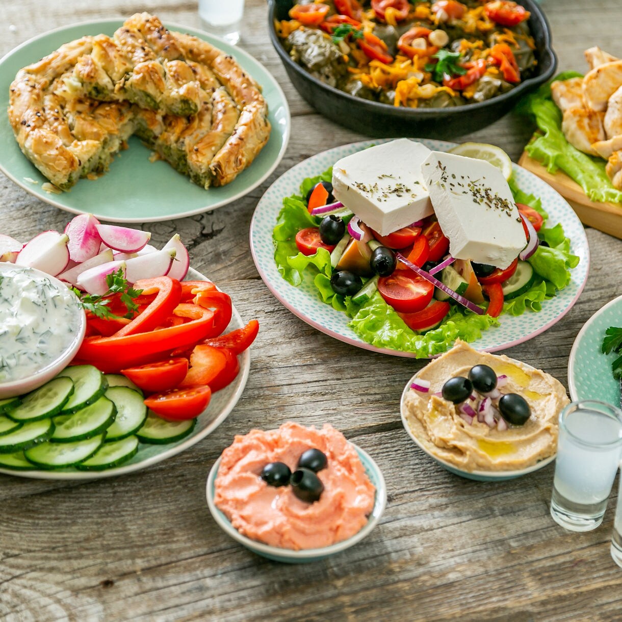 Greek meze feast on a rustic table with grilled fish, feta salad, tzatziki, hummus, pita bread, and vegetables.
