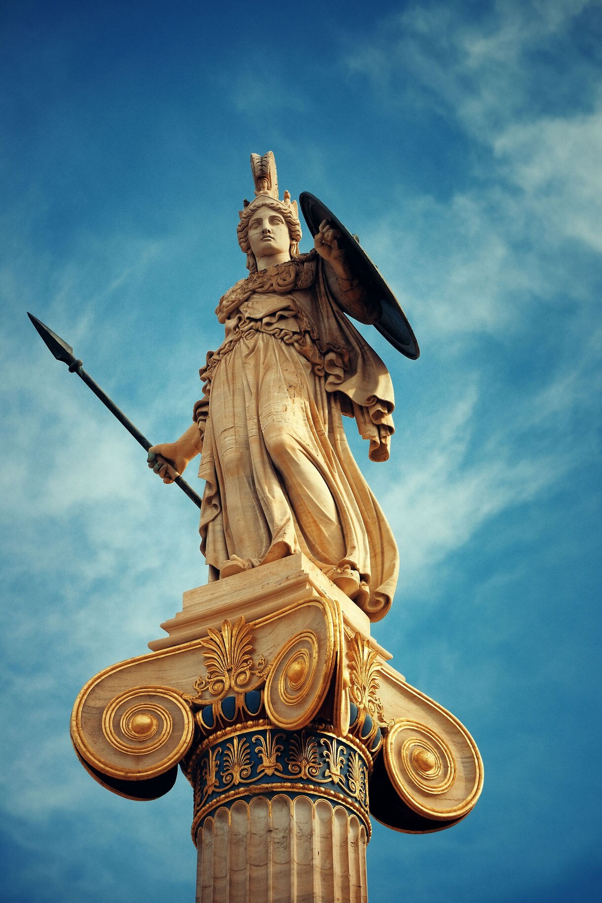 Marble statue of Athena holding a spear and shield atop an ornate column against a blue sky.