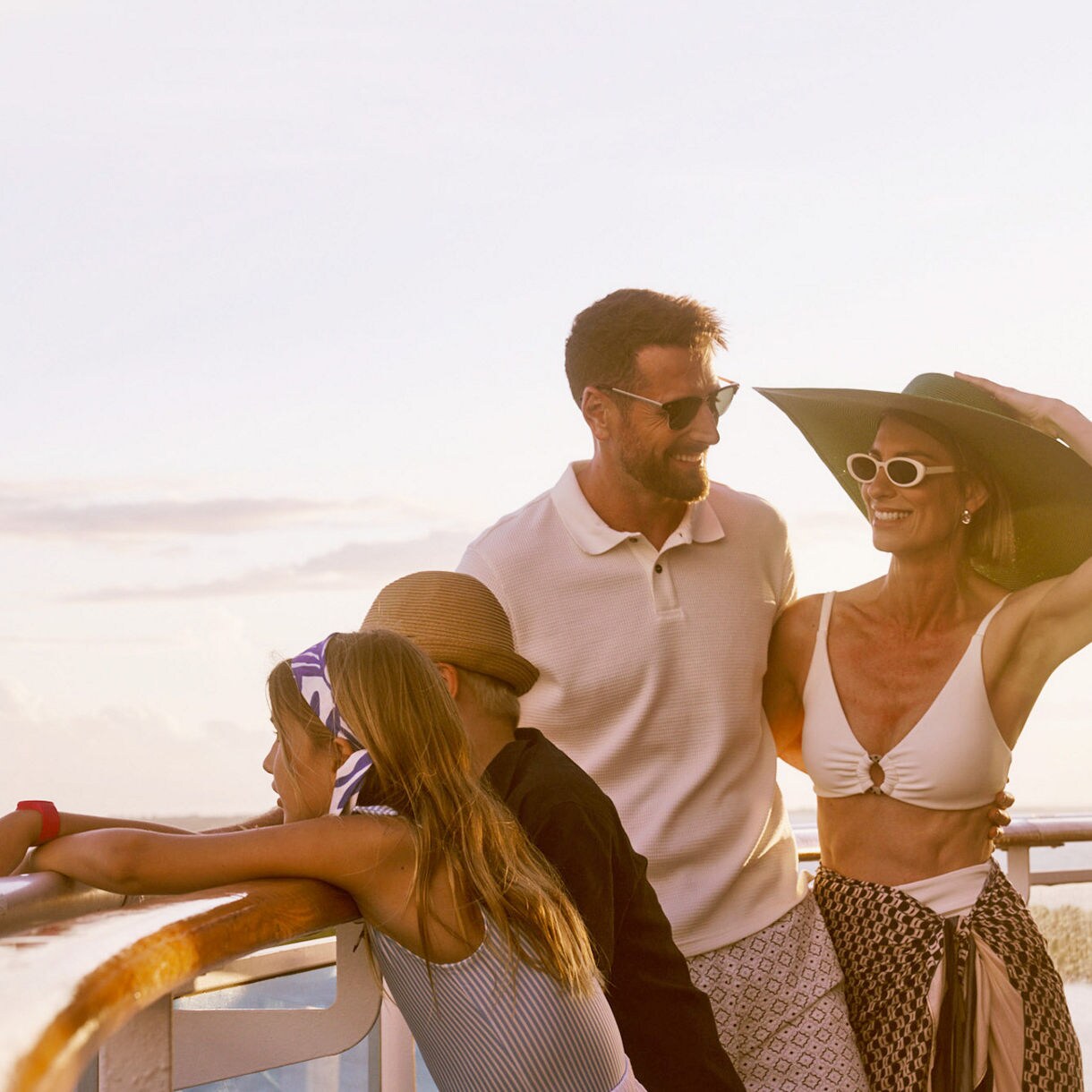 Family on ship deck rail at sunset