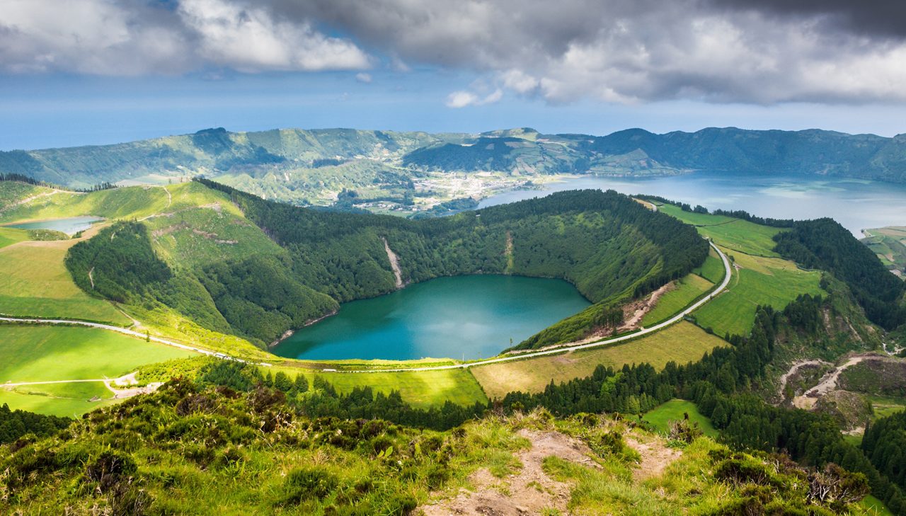 Panoramic view of Lagoa de Santiago, a deep green crater lake surrounded by lush hills and winding roads.