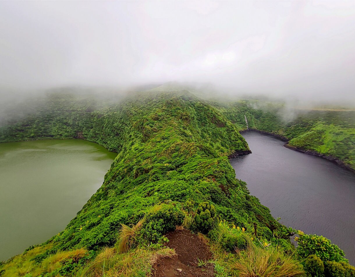 Foggy aerial view of Lagoa das Empadadas on São Miguel Island showing two crater lakes separated by a narrow, green-covered ridge.