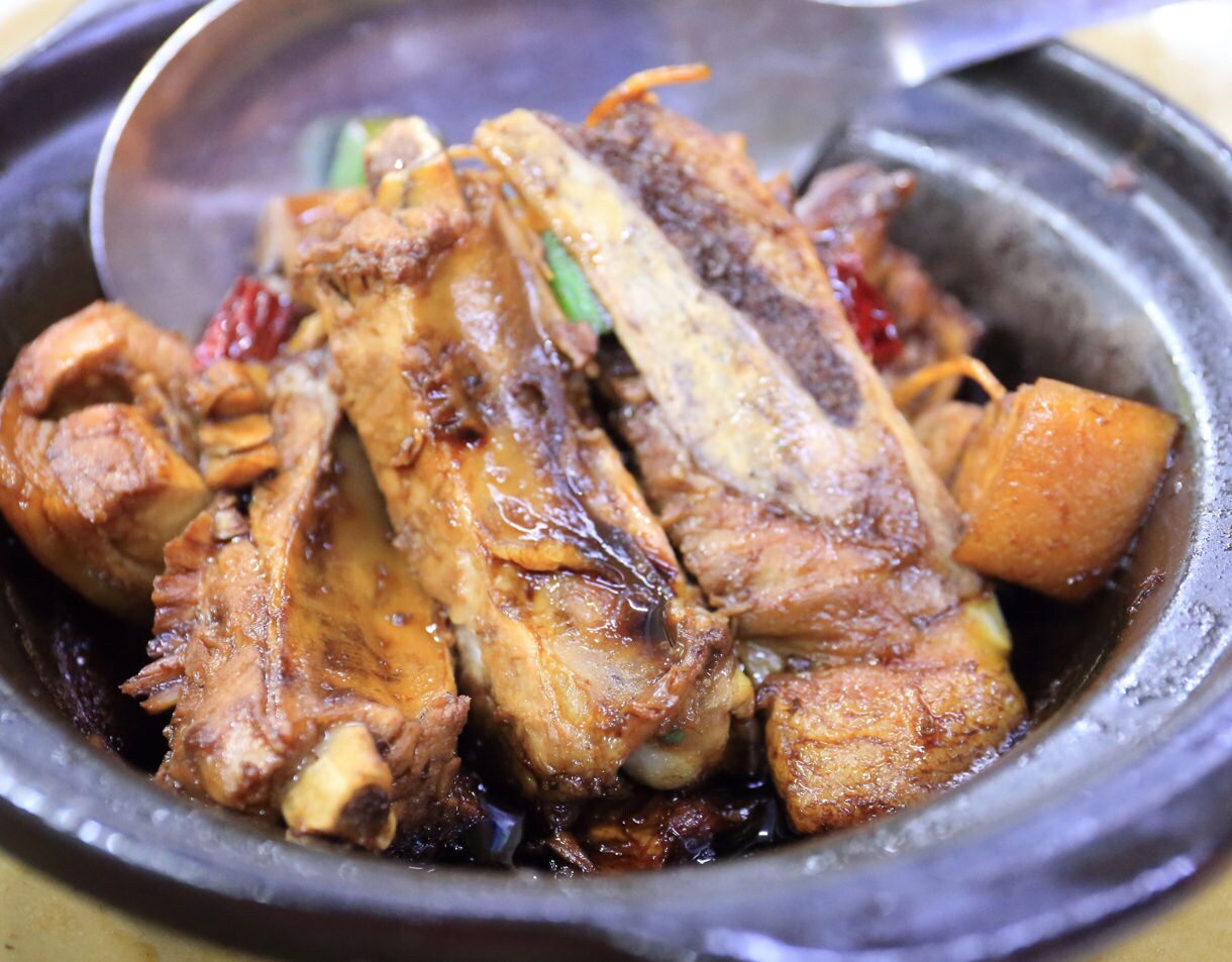 Close-up of Bak Kut Teh served in a clay pot with tender pork ribs, tofu and herbs in rich dark broth.