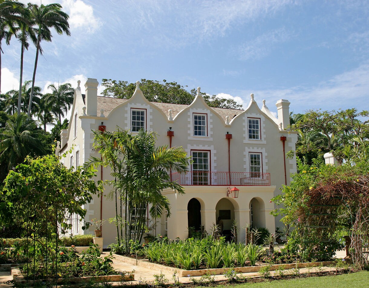 Historic Jacobean-style plantation house at St. Nicholas Abbey in Barbados, featuring gabled rooftops, arched entryways and tropical gardens filled with greenery and palm trees.
