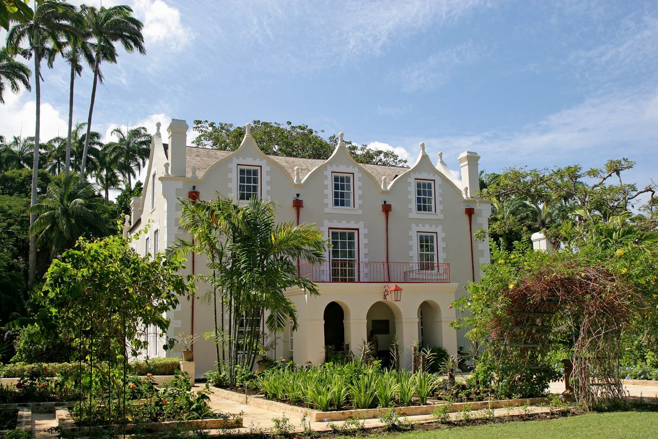 Historic Jacobean-style plantation house at St. Nicholas Abbey in Barbados, featuring gabled rooftops, arched entryways and tropical gardens filled with greenery and palm trees.