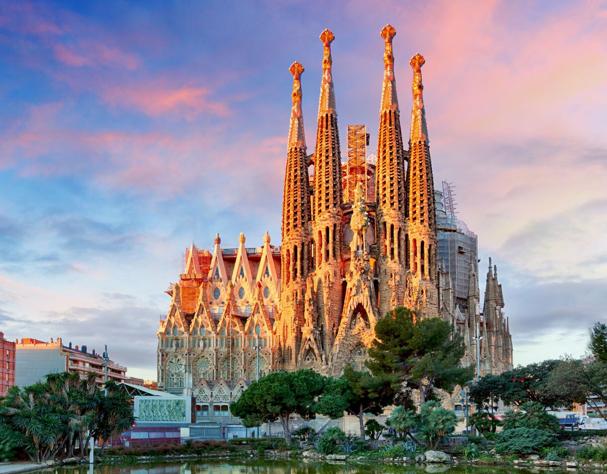 The Sagrada Família basilica in Barcelona illuminated by sunset, its soaring spires framed by pink and blue clouds above.