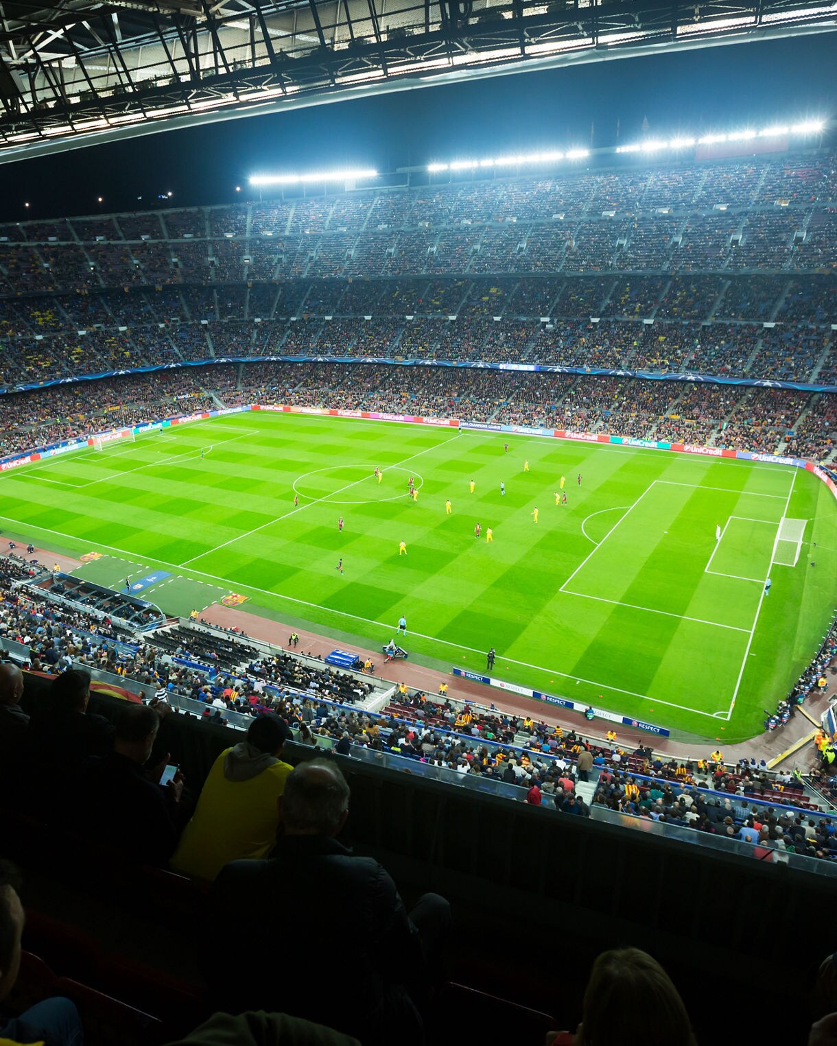 A packed Camp Nou stadium in Barcelona at night, with fans filling the stands and players in action on the brightly lit pitch.