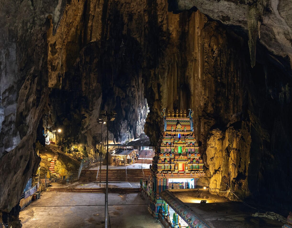 Interior of Batu Caves in Malaysia with a brightly painted Hindu temple and steep stone walls rising above.
