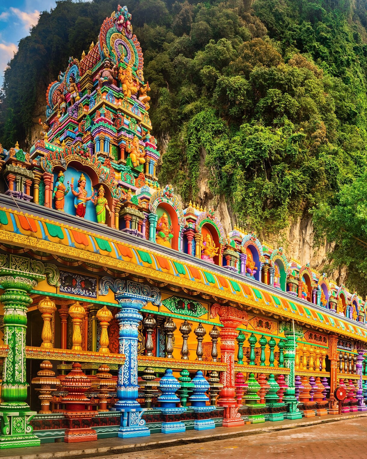 Batu Caves entrance in Malaysia featuring colorful temple structures, rainbow staircase and giant golden Lord Murugan statue.