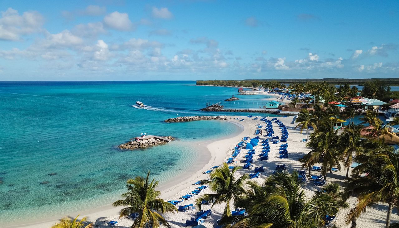 Aerial view of Princess Cays showing white sand beach lined with blue beach chairs, turquoise Caribbean waters, palm trees, and tropical facilities.