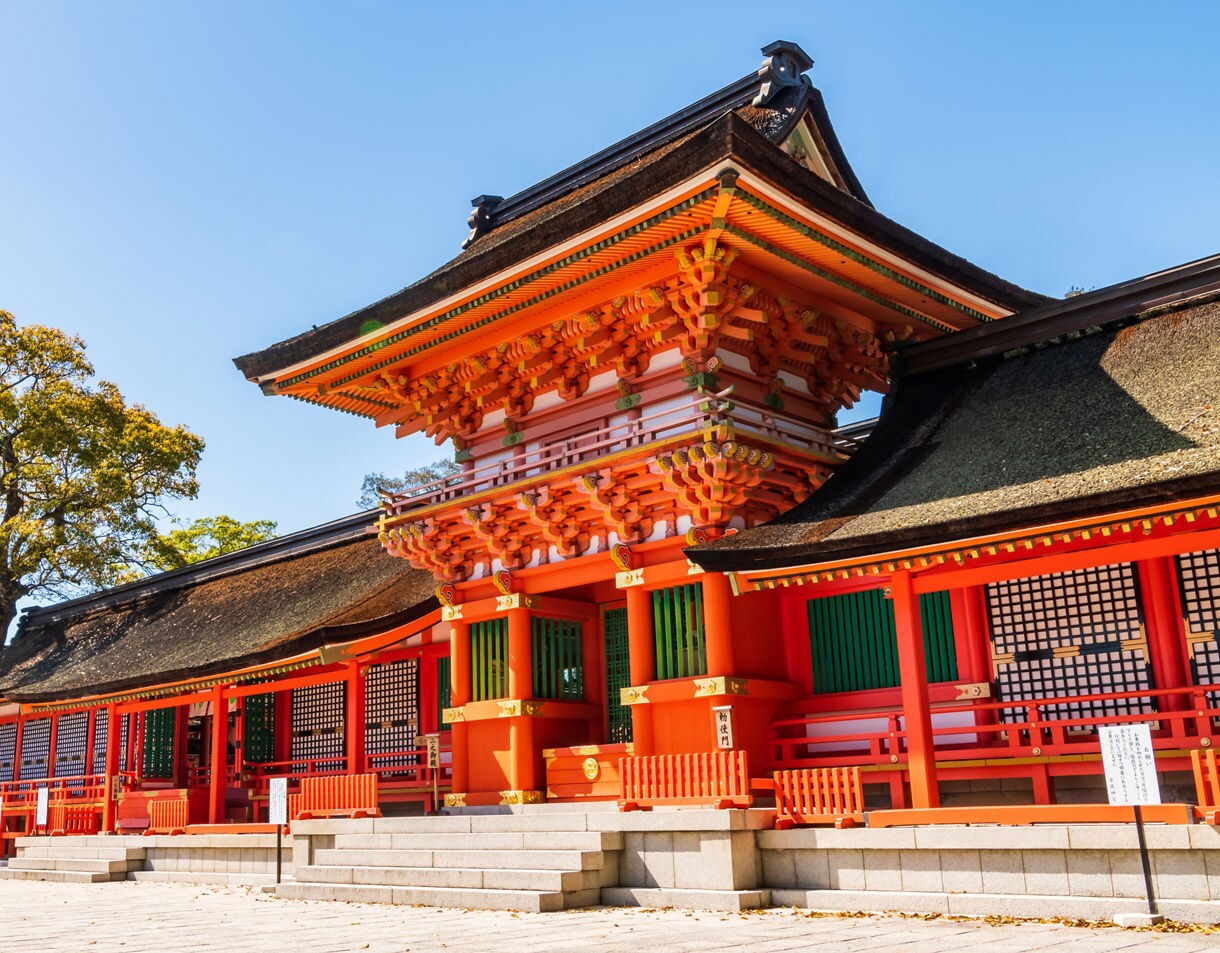 Bright red and orange shrine buildings at Usa Jingu in Beppu, Japan, featuring ornate woodwork, green shutters and a clear blue sky.
