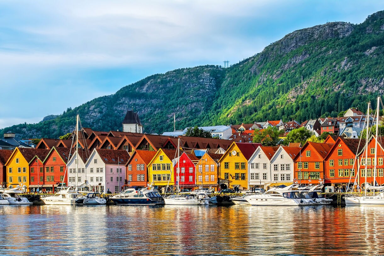 Brightly painted historic wooden buildings of Bryggen Wharf in Bergen, Norway, reflected in the harbor with boats moored in front.