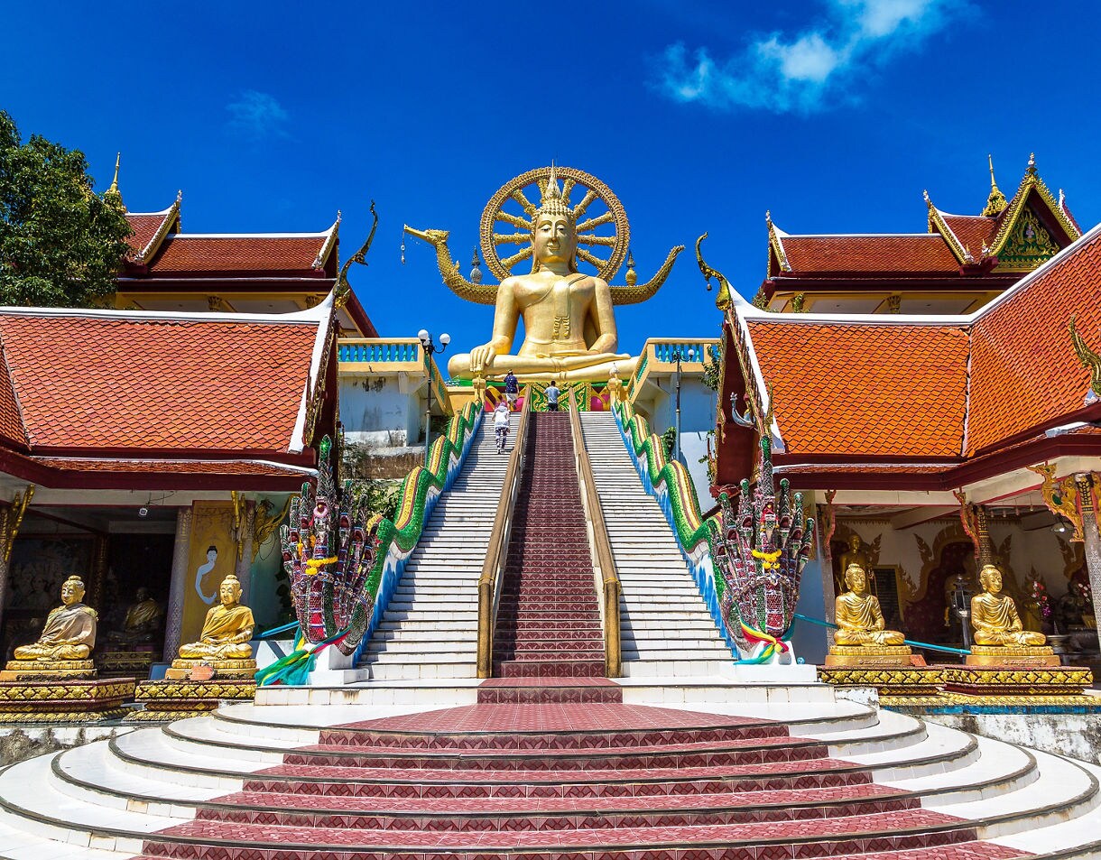 Golden seated Buddha statue atop a grand staircase flanked by colorful naga serpents at the Big Buddha Temple in Koh Samui.