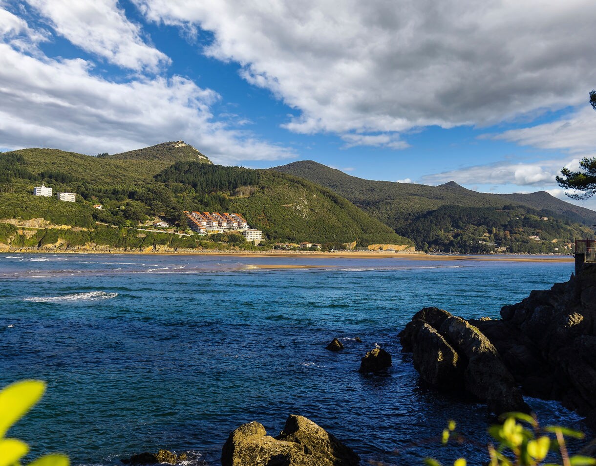 Scenic view of Biscay Bay with blue waters, rocky shoreline and forested hills dotted with small buildings under a partly cloudy sky.