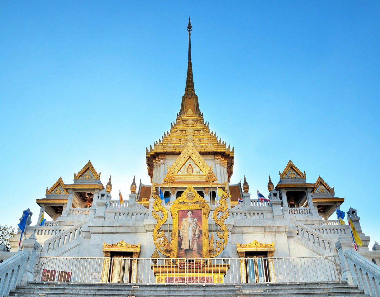 Ornate white and gold temple with steep stairs leading up to spired rooftops, featuring a framed portrait above the entrance.