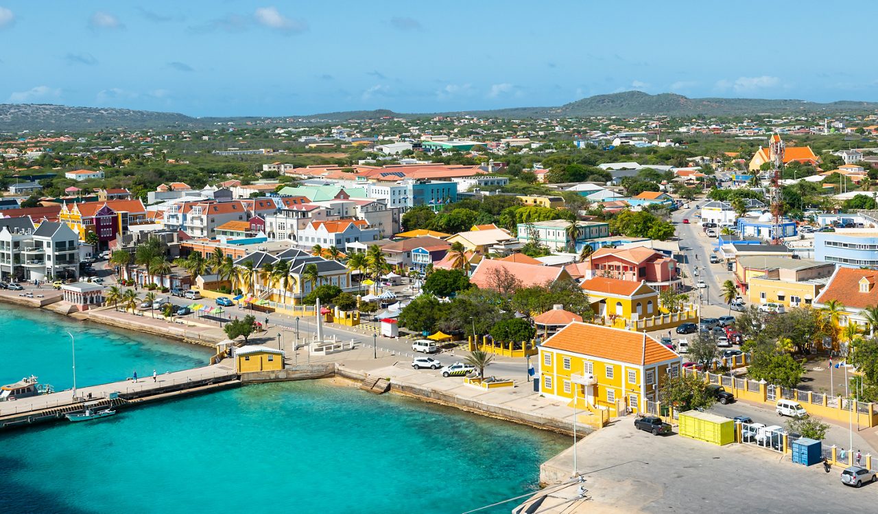 Aerial view of Kralendijk, Bonaire’s waterfront featuring pastel-colored Dutch-Caribbean buildings, a turquoise shoreline, and a bustling town with shops and restaurants.