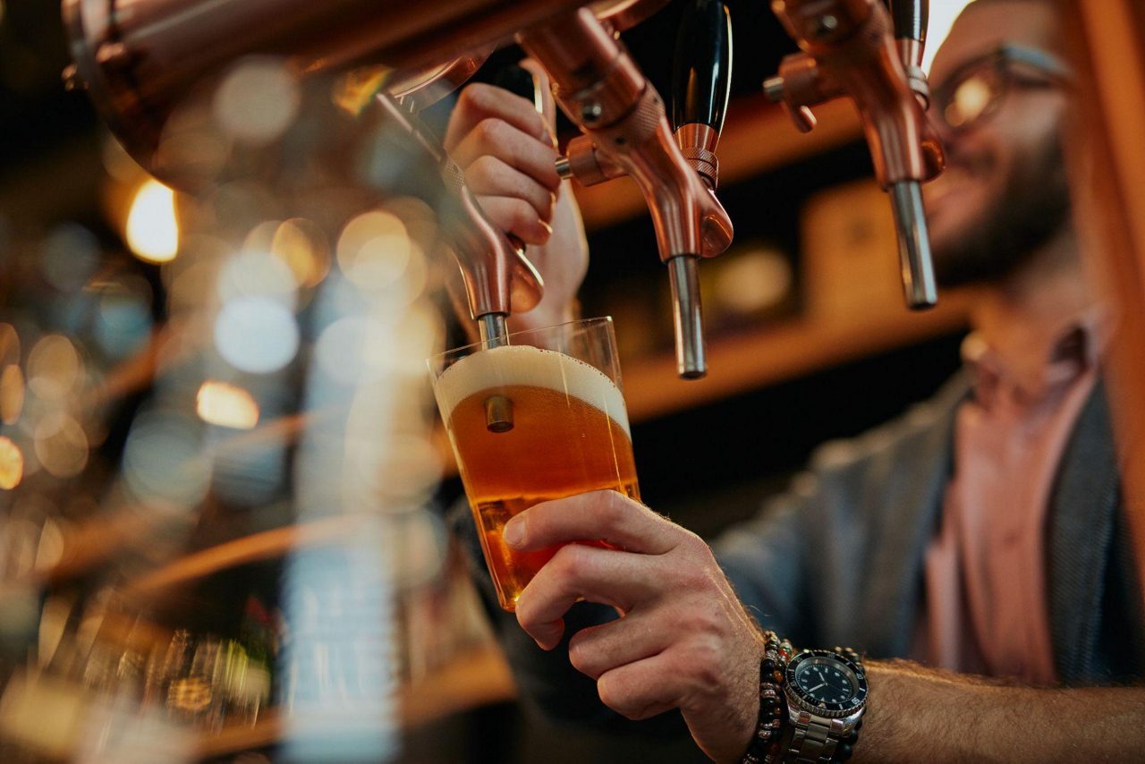 Close-up of a bartender filling a pint glass with beer from a tap, with golden foam forming at the top.