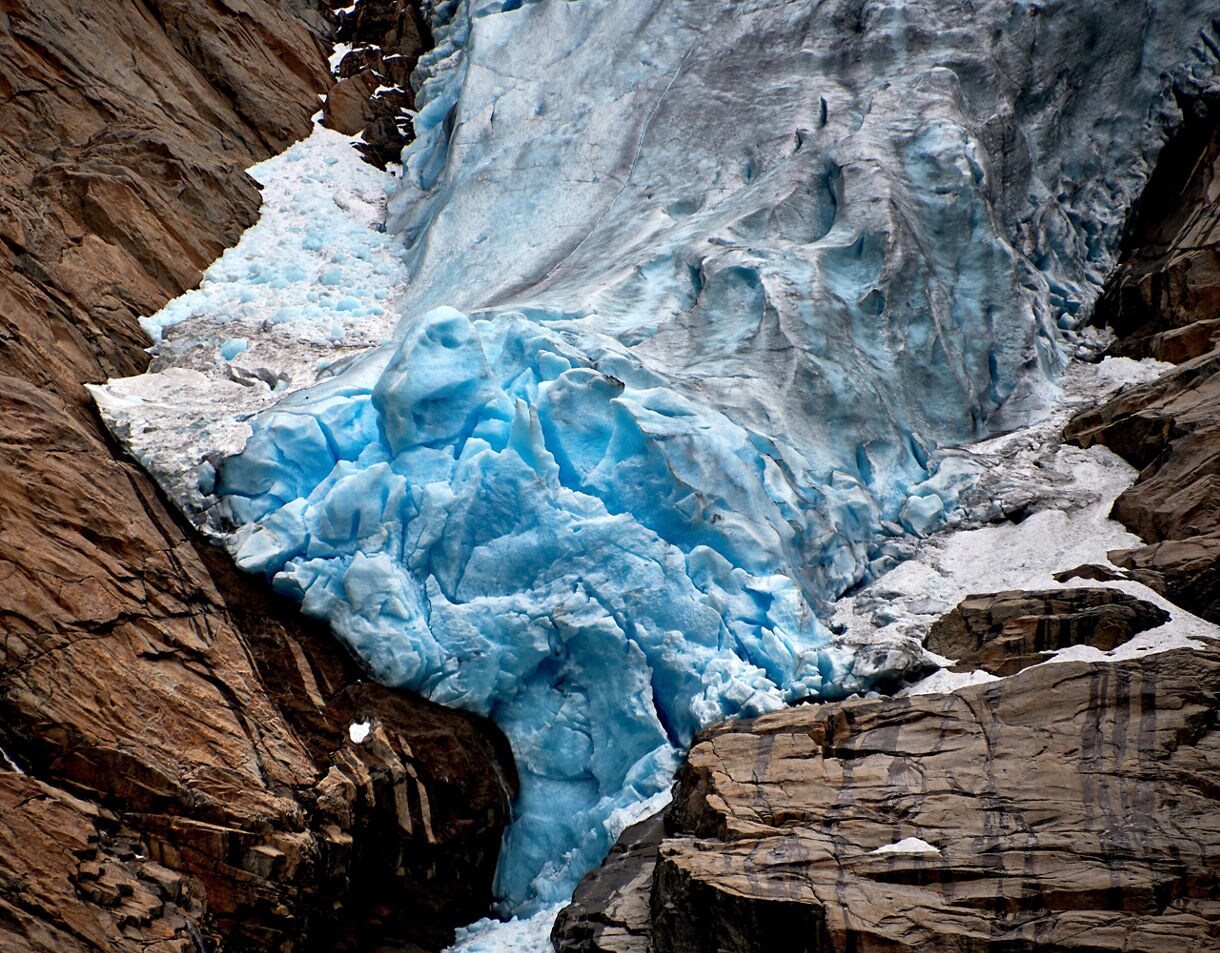 Close-up view of Briksdal Glacier in Norway, showing bright blue ice pressed against brown rocky cliffs.