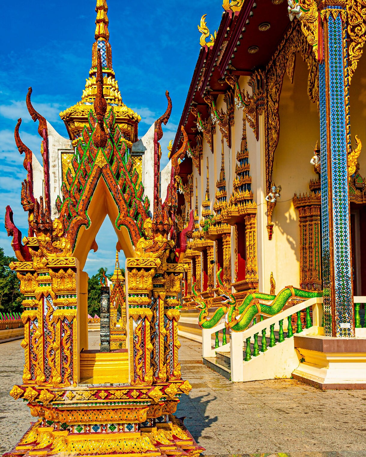 Close-up of an elaborately decorated Thai Buddhist temple with golden spires, green serpent motifs and colorful mosaic details.