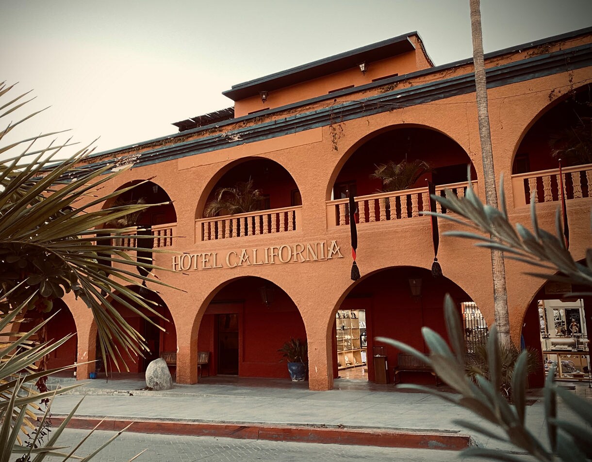 Exterior of Hotel California in Todos Santos featuring terracotta arches, a second-story balcony with plants and a bold sign above the entrance.