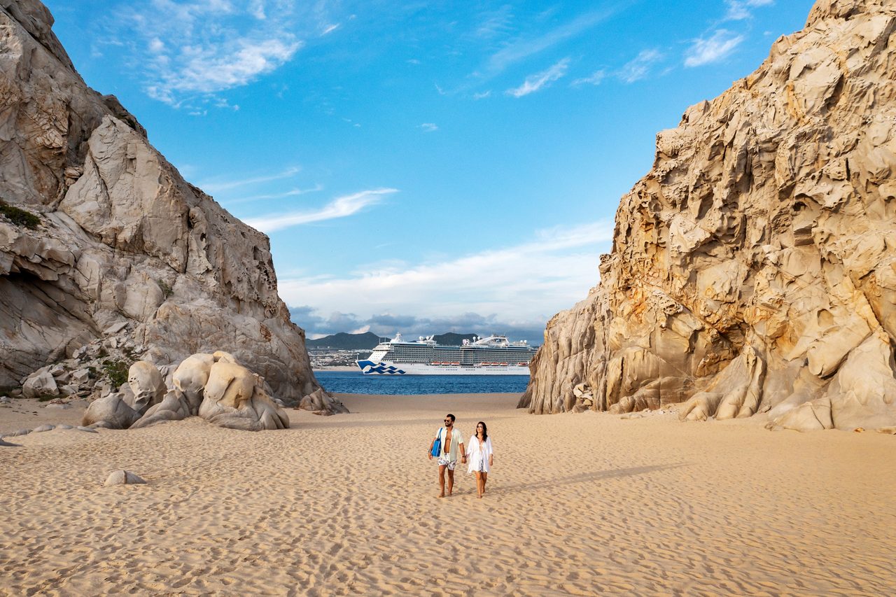 Couple walking on empty beach with a Princess ship in the background. Cabo San Lucas.