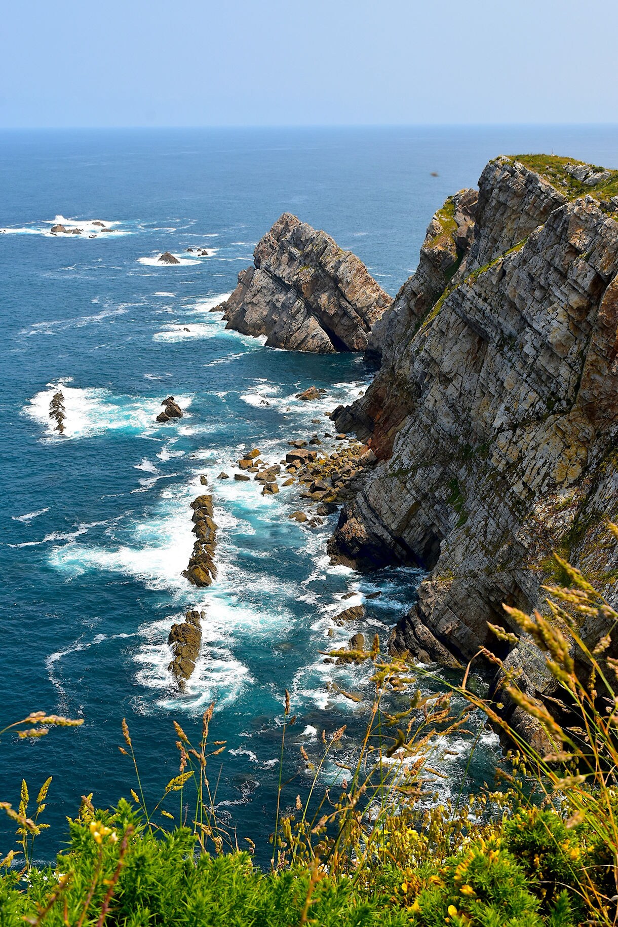 Steep rocky cliffs along the Cabo coastline with jagged formations and white-capped waves breaking against the shore.