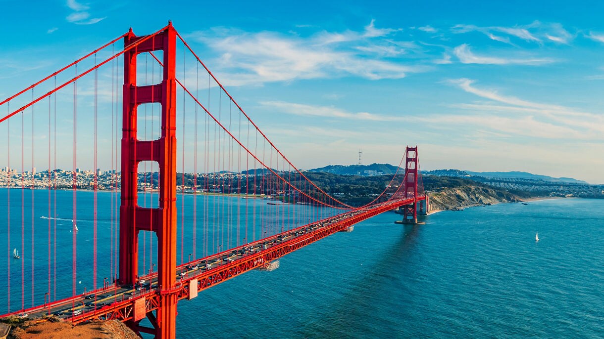 The Golden Gate Bridge towering over the blue waters, with San Francisco's skyline in the background and hills surrounding the bay.