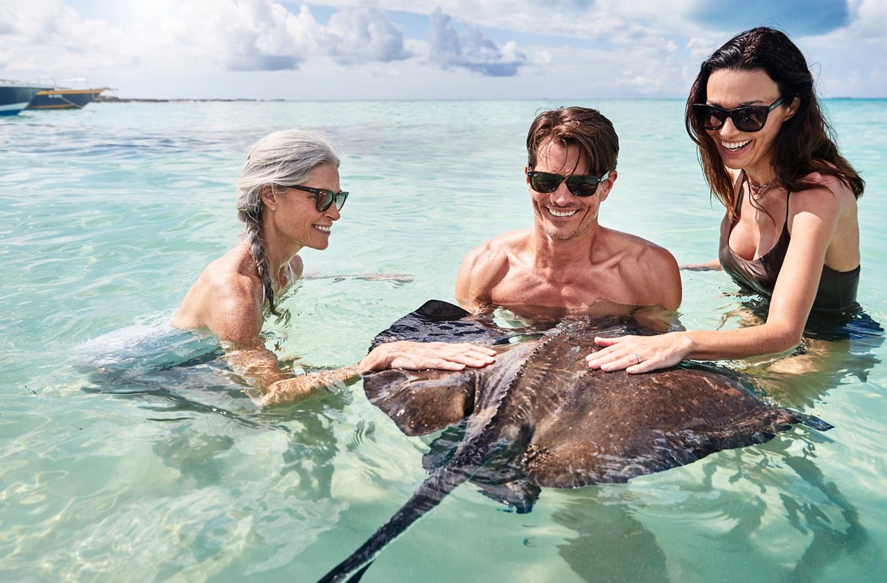 Two people enjoying swimming in clear turquoise water, appearing relaxed and happy while partially submerged.