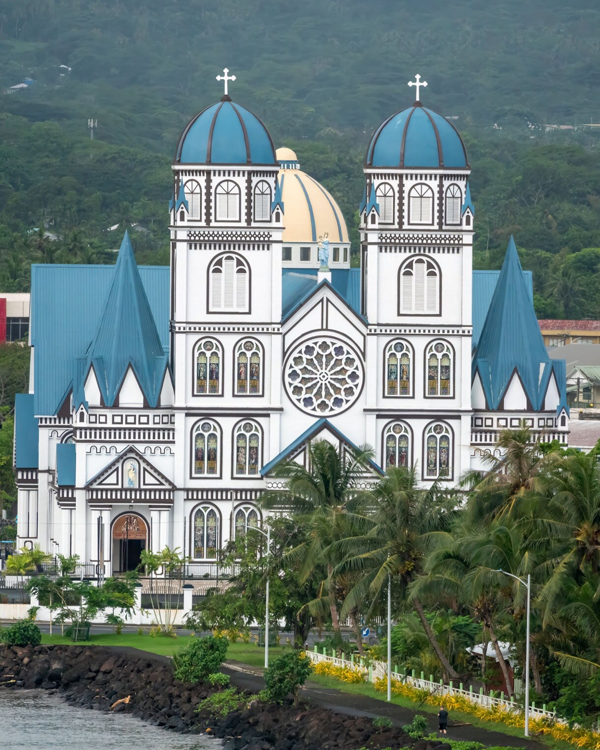 The Cathedral of the Immaculate Conception in Apia with twin blue domes, stained glass window and lush palm trees along the waterfront.