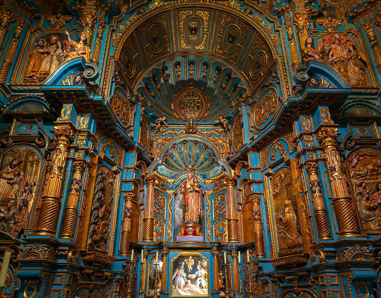 Highly detailed baroque altar inside the Cathedral of Lima, featuring turquoise panels, gold trim, carved religious scenes and a central statue beneath a domed, ornate canopy.