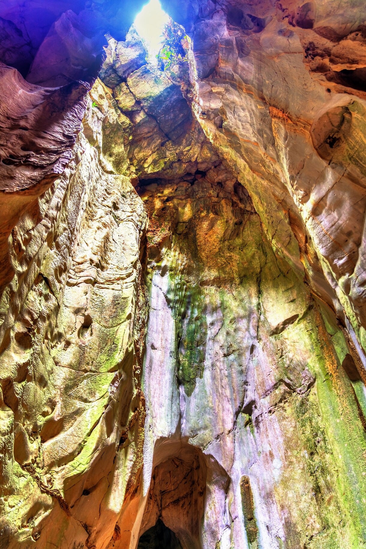 View looking upward inside a Marble Mountains cave, showing textured rock walls bathed in green and gold light with sunlight filtering through an opening above.