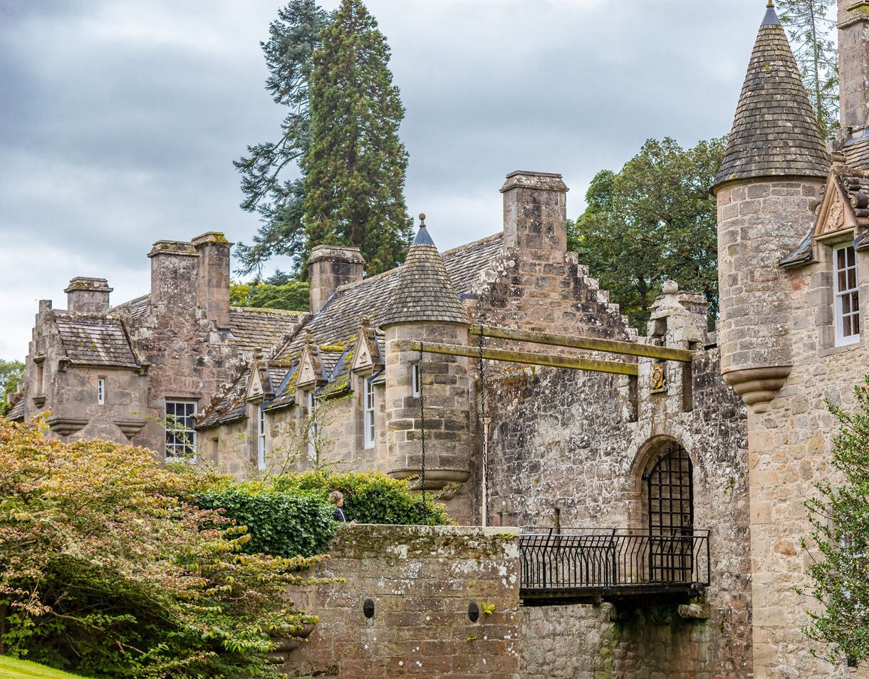 Close-up of Cawdor Castle’s stone facade with turrets, chimneys and a drawbridge leading into the main entrance.