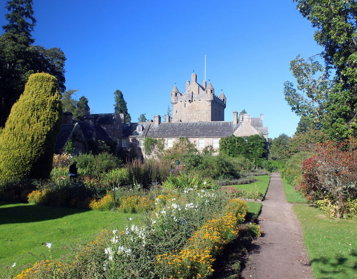 Cawdor Castle in Scotland with lush gardens full of colorful flowers and manicured greenery under a clear blue sky.