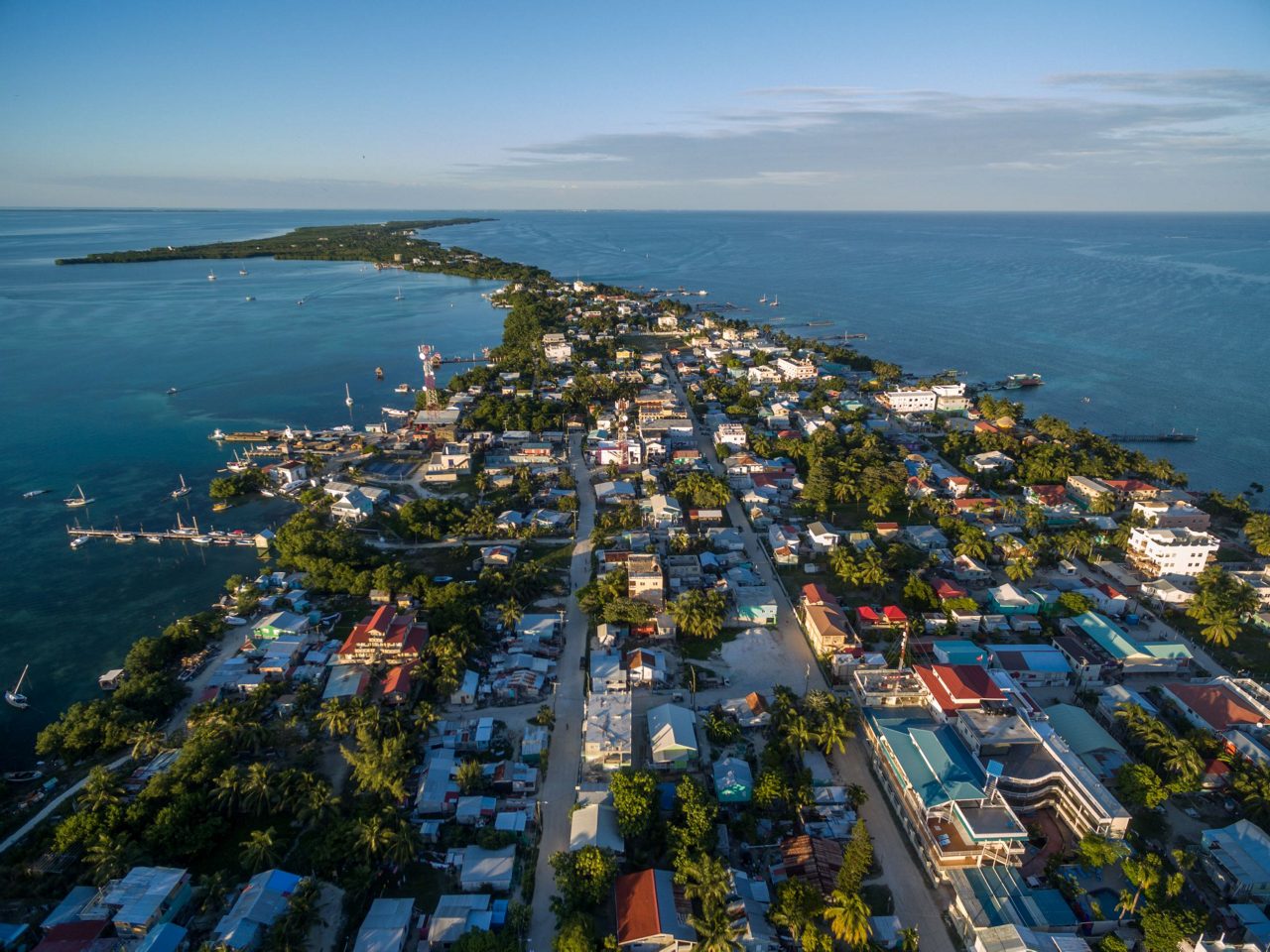 Aerial view of Caye Caulker island in Belize showing colorful buildings, main street, and boats anchored in turquoise Caribbean waters.