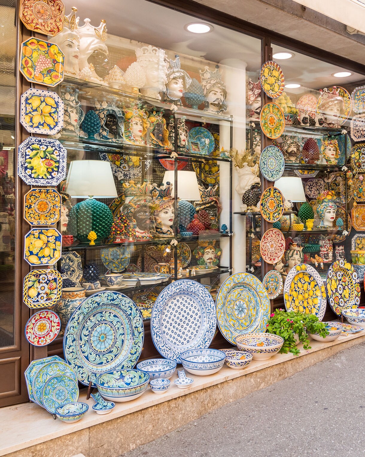 Colorful ceramic plates and pottery displayed outside a Sicilian shop, arranged along the wall and storefront shelves.