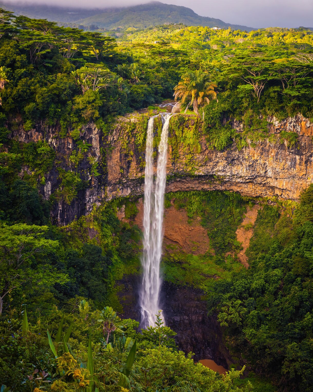 Tall waterfall dropping from a cliff surrounded by dense tropical forest.