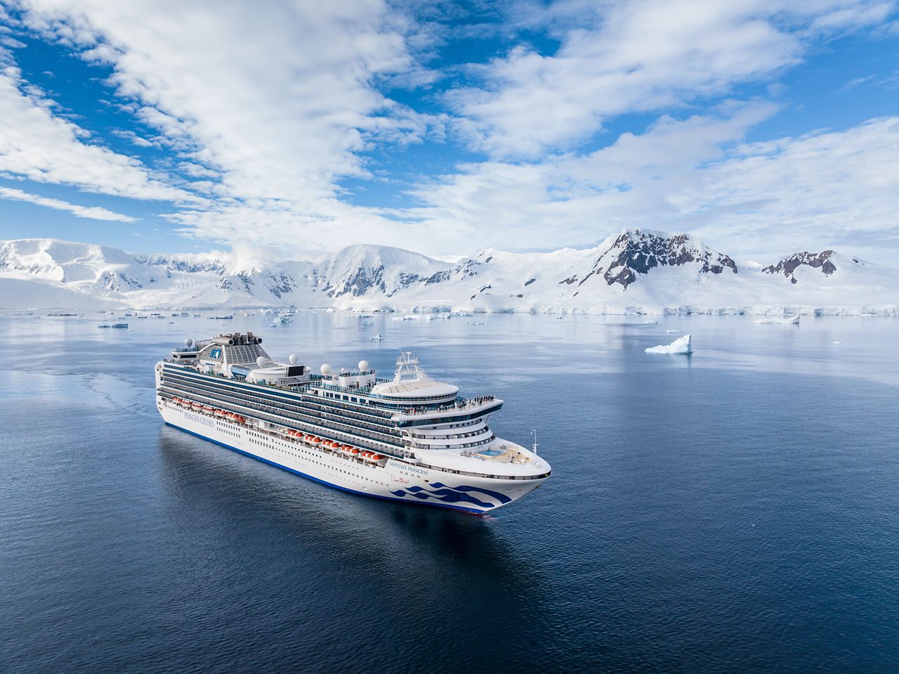 A Princess Cruises ship, the Sapphire Princess, sailing in Antarctica with snow-covered mountains and icebergs in the background, set against a clear blue sky and tranquil waters.