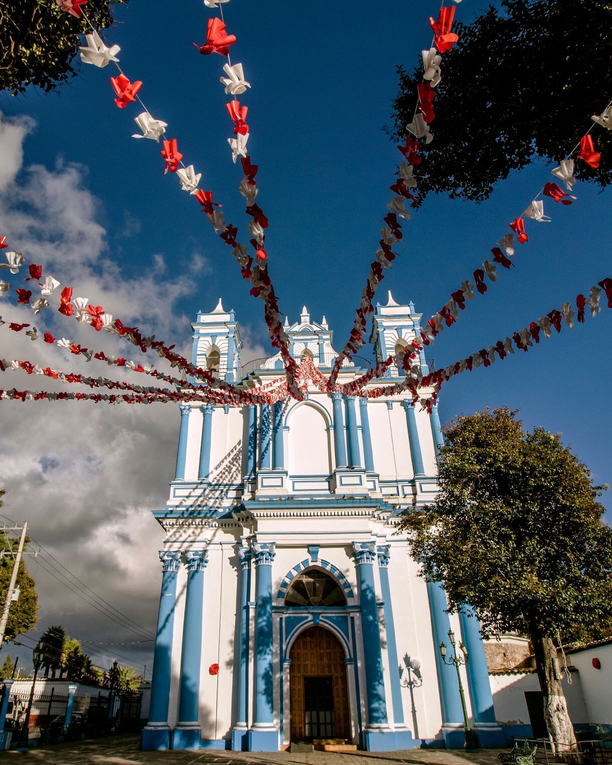Blue and white colonial-style church in Tapachula, Chiapas, decorated with red and white festoon banners stretching outward against a bright sky.